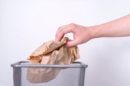 A hand throws a crumpled paper bag into a trash can. The concept of the environmentの写真素材