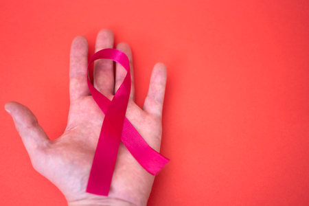 A hand holding a red ribbon about AIDS on a red background. The concept of World AIDS Day on December 1.の写真素材