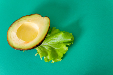 Half avocado and green lettuce leaf on green background with space for text. The concept of healthy...