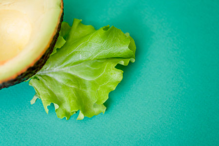Half avocado and green lettuce leaf on green background with space for text. The concept of healthy...