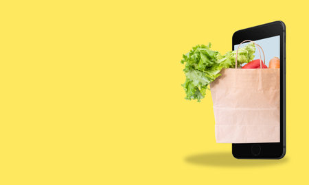 Modern art collage cell phone grocery bag on yellow background with space for text. Delivery service concept, online shopping, food, technology. ad space.の写真素材