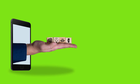 Digital art collage, the hand with wooden cubes coming out of the phone on a green background. environmental products. The concept of using clean systems.の写真素材