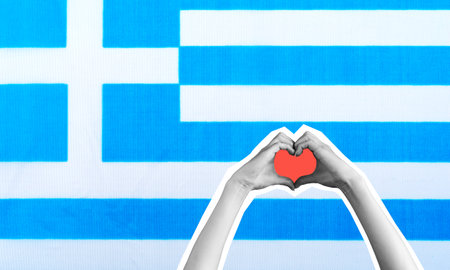 A modern artistic collage featuring hands forming a heart shape against the background of the Greek flag. The concept conveys travel and leisure in Greece.の写真素材