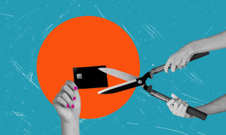A hand holds a credit card as another hand holding a pair of pruning shears comes in to cut it. The image is set against a blue and orange background.の写真素材