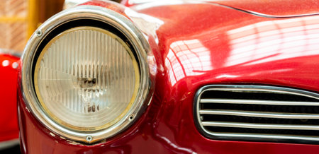 Bright red vintage car headlight illuminates the interior of a museum, highlighting the craftsmanship and design of classic automobiles from a bygone era.の写真素材