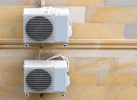 Two air conditioning units are securely installed on a stone wall, showing a functional design. The setting is residential, and the natural light highlights the textures of the surface.の写真素材