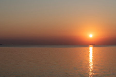 The sun sets on the horizon, casting golden hues across the tranquil water. A peaceful ambiance envelops the scene as the day concludes in this relaxing coastal location.の写真素材