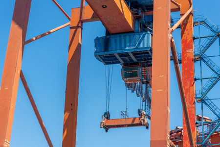 A large crane towers in a port setting, with its bright orange structure contrasted against a clear...