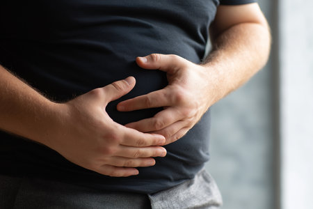 A man stands indoors with his hands on his stomach. He appears to be experiencing discomfort. The scene takes place in the morning with natural light coming through.の素材