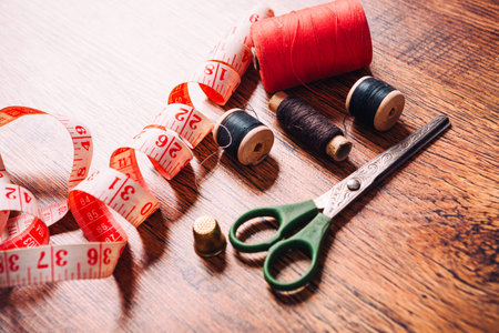 tailor the tool to measure the length,  scissors, spools of colored thread on a wooden background