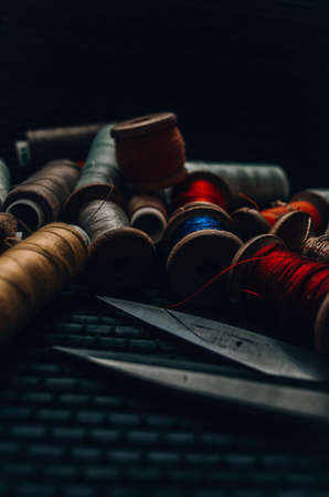 Retro sewing items: tailoring scissors, cutting knife, thimble, wooden thread spools, cushion for including pins, fabrics and sewing accessories.の写真素材