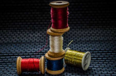 Retro sewing items: tailoring scissors, cutting knife, thimble, wooden thread spools, cushion for including pins, fabrics and sewing accessories.の写真素材