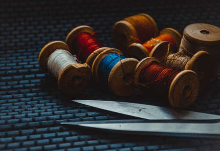 Retro sewing items: tailoring scissors, cutting knife, thimble, wooden thread spools, cushion for including pins, fabrics and sewing accessories.の写真素材