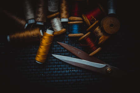 Retro sewing items: tailoring scissors, cutting knife, thimble, wooden thread spools, cushion for including pins, fabrics and sewing accessories.の写真素材