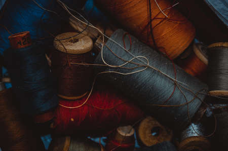 Retro sewing items: tailoring scissors, cutting knife, thimble, wooden thread spools, cushion for including pins, fabrics and sewing accessories.の写真素材
