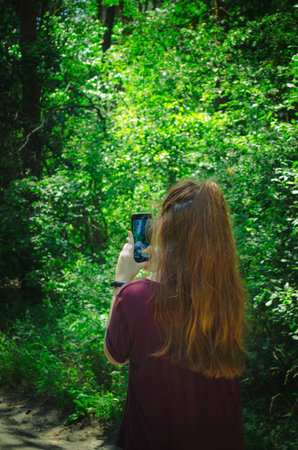 young girl blogging in the forest, taking pictures of nature