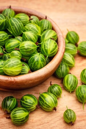 Old Wooden Bowl Filled With Succulent Juicy Fresh Ripe Green Gooseberries On An Old Wooden Table Top.の写真素材