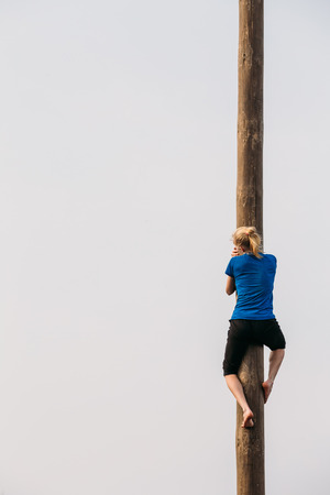 GOMEL, BELARUS - February 21, 2014: Young woman climbs on a wooden post on the traditional holiday dedicated to the approach of spring - Slavic celebration Shrovetide.のeditorial素材