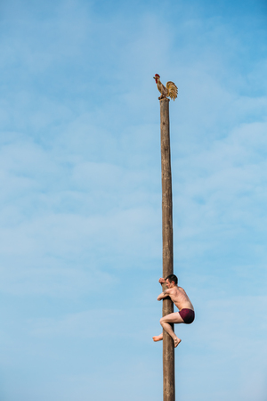 GOMEL, BELARUS - February 21, 2014: Young man climbs on a wooden post on the traditional holiday dedicated to the approach of spring - Slavic celebration Shrovetide.のeditorial素材