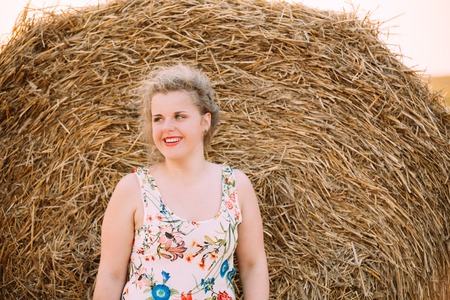 Beautiful Plus Size Young Woman In Shirt Posing In Summer Field Meadow Near Hay Bales At Sunset Backgroundの写真素材