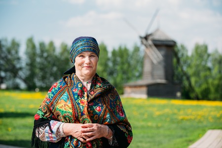SUZDAL, RUSSIA - May 22, 2015: Russian woman in traditional Russian dress and scarf on the background of an old wooden mill.のeditorial素材