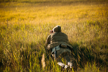 Unidentified re-enactor dressed as Soviet soldier scout looks at an old army binoculars.