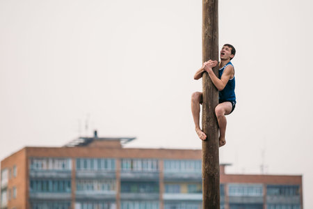 GOMEL, BELARUS - February 21, 2014: Young man climbs on a wooden post on the traditional holiday dedicated to the approach of spring - Slavic celebration Shrovetide.のeditorial素材