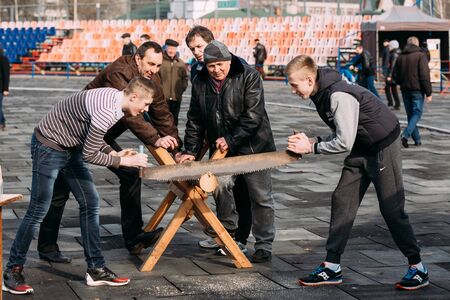 Gomel, Belarus - March 12, 2016: Young men sawing a tree trunk on a traditional holiday fun at  Celebration of Maslenitsa Shrovetide holiday.のeditorial素材