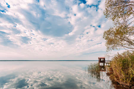 Old Wooden Pier For Fishing, Small House Or Shed And Beautiful Lake Or River In Background.の写真素材