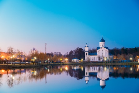 Evening View Of Alexander Nevsky Orthodox Temple Church Behind City Lake. Evening Illumination Of Residential Area And Park Reflecting In Water Surface. The Early Spring In Gomel Homiel Belarusの写真素材