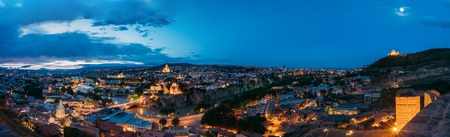 Tbilisi, Georgia. The Scenic Panoramic Top Field Of Vision. Cityscape In Evening Illumination With All Famous Landmarks And Sights Under Dramatic Blue Sky With Moon Background.の写真素材