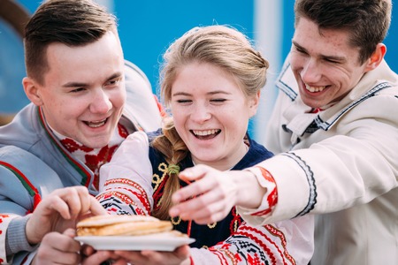 Gomel, Belarus - March 12, 2016: Happy young people dressed in national folk clothes posing with a plate of pancakes in hands at traditional folk Celebration of Maslenitsa Shrovetide holidayのeditorial素材