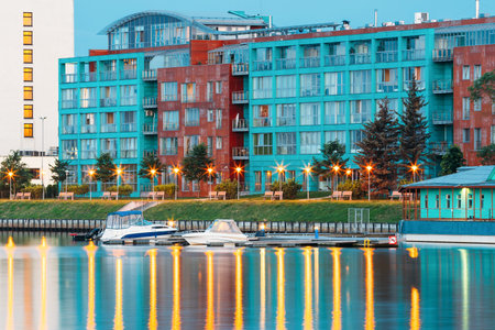 Riga, Latvia. Old Building At Evening Illuminated Embankment And Pier Of Daugava River In Summer Dusk.の写真素材