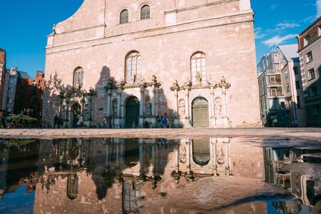 Riga, Latvia. The Facade Of St. Peter Church With Three Identical Portals And Its Reflection In The Puddle Of Rain Water In Sunny Summer Day, Blue Sky.の写真素材