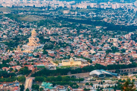 Tbilisi, Georgia. Evening Aerial Panoramic View Of Sameba Complex, Holy Trinity Cathedral Surrounded By Populous Residential Area In Summer Dusk.の写真素材