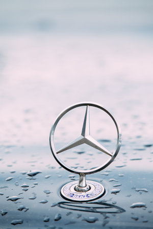 Close View Of Metal Star Logo Of Mercedes Benz At Wet Hood Of Blue