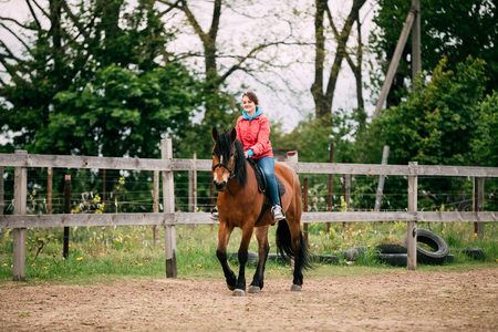 Young Smiling Caucasian Woman Riding The Brown Horse On Countrysideの写真素材