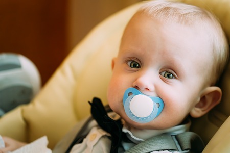 Pretty Baby Boy Sitting In Yellow Seat With Sootherの写真素材
