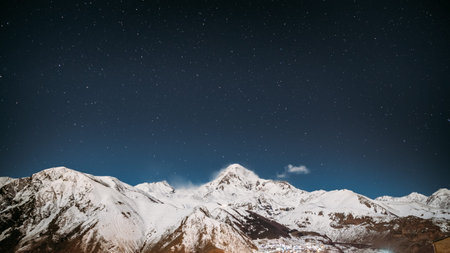 Georgia. Winter Night Starry Sky With Glowing Stars Over Peak Of Mount Kazbek Covered With Snow....