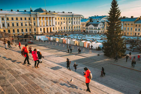 Helsinki, Finland. Woman Tourist Taking Picture Of Seagull Bird Near Christmas Xmas Market With Christmas Tree On Senate Square In Sunny Winter Day.のeditorial素材