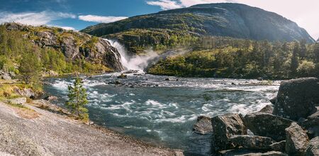 Kinsarvik, Hordaland, Norway. Waterfall Nykkjesoyfossen In Hardangervidda Mountain Plateau. Summer Sunny Day. Height Of 49 M. Famous Landmark And Popular Destination. Panorama, Panoramic Viewの写真素材