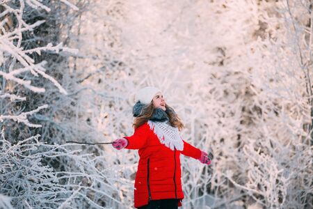 Young Beautiful Pretty Caucasian Girl Woman Dressed In Red Jacket And White Hat Smiling And Enjoying Life In Snowy Forest In Winter Dayの写真素材