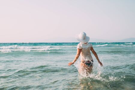 Young Caucasian Lady Woman In Swimsuit And Summer Hat Walking In Sea. Vacation On Sea Ocean Beachの写真素材