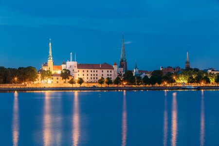 Riga, Latvia. Panoramic Picturesque Urban View Of Daugava Or Western Dvina River In Central Part Of City With Famous Landmarks In Bright Illumination Under Blue Sky In Summer Night.の写真素材