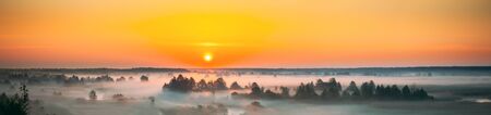Amazing Sunrise Sunset Over Misty Landscape. Scenic View Of Foggy Morning Sky With Rising Sun Above Misty Forest And River. Early Summer Nature Of Eastern Europe. Panorama.の写真素材