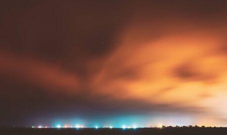Night Sky With Rare Glowing Stars Shining Through The Cloudiness Overcast Above Countryside Town Landscape. Rural Field Meadow In Early Spring.の写真素材