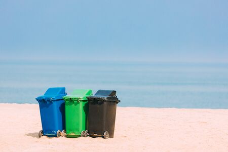 Three Plastic Waste Containers On Wheels For Separate Collection Of Garbage. Containers For Temporarily Storing Waste. Dustbins, Garbage Cans, Trash Cans On Sea Ocean Coast Beach.の写真素材
