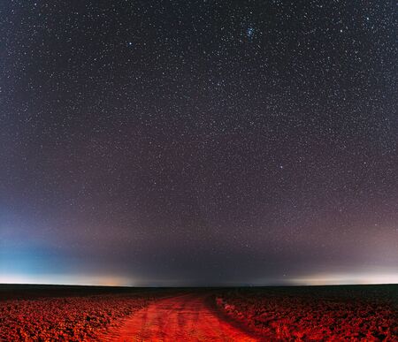 Night Starry Sky With Glowing Stars Above Country Road Is Lit In Red. Countryside Field Landscape.の写真素材