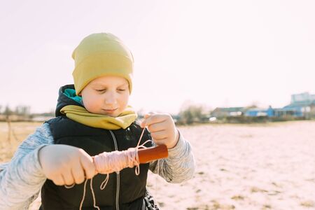 Boy Of 6-7 Years Old Takes Up A Twine From A Kite. Pleasant Activity In Fresh Air On A Sunny Spring Or Autumn Dayの写真素材