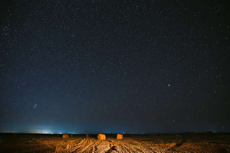 Night Starry Sky Above Haystacks In Summer Agricultural Field. Night Stars Above Rural Landscape With Hay Bales After Harvest. Agricultural Conceptの写真素材